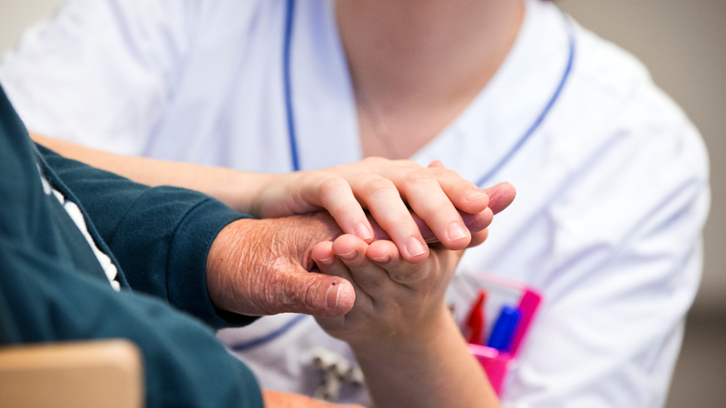 Vårdpersonal håller patients hand.