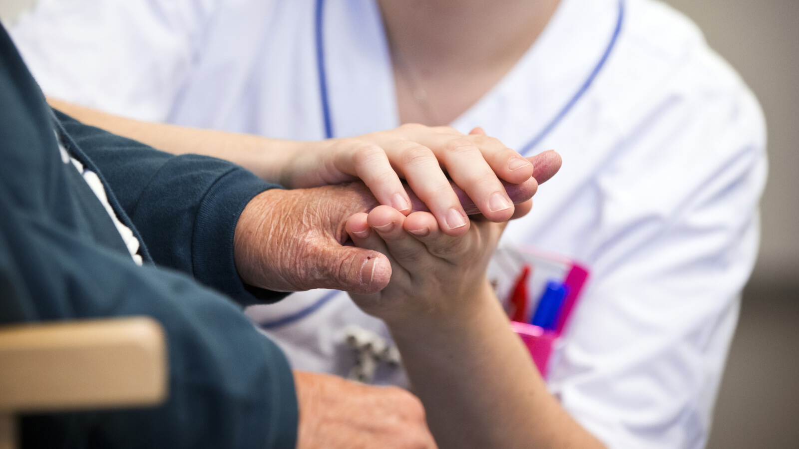 Vårdpersonal håller en patients händer mellan sina. 