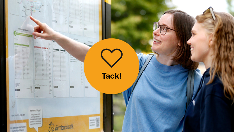 Två kvinnor utomhus tittar på tidtabell på anslagstavla. Ett gult hjärta som det står Tack ligger framför fotot.
