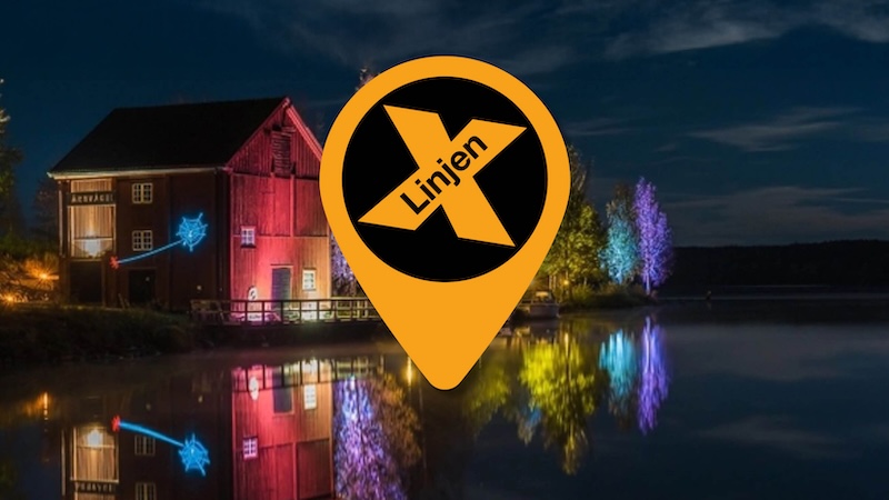 Ljusbelyst byggnad vid vattnet i Borgvik med X‑linjens symbol i förgrunden.
