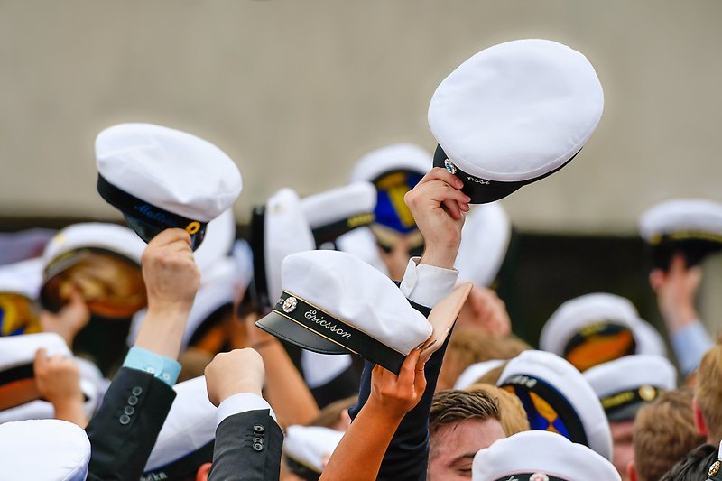 Händer som håller upp studentmössor