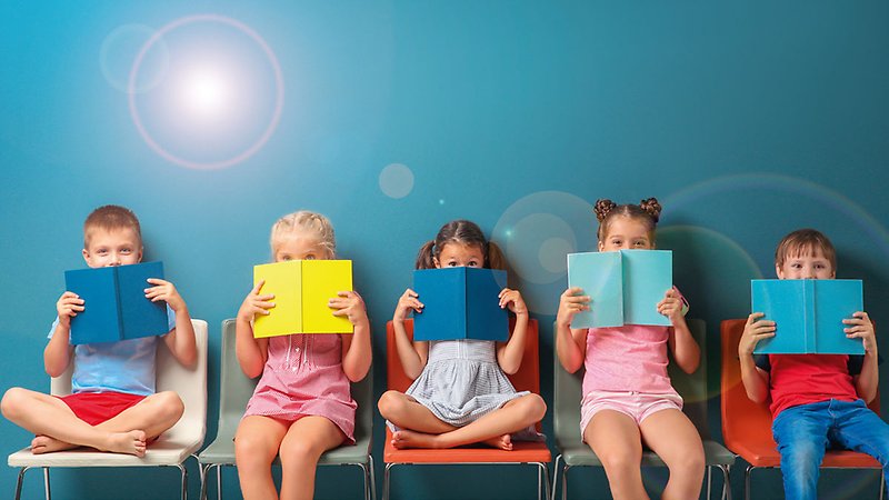 Fem barn med färglada böcker framfrö ansiktet.